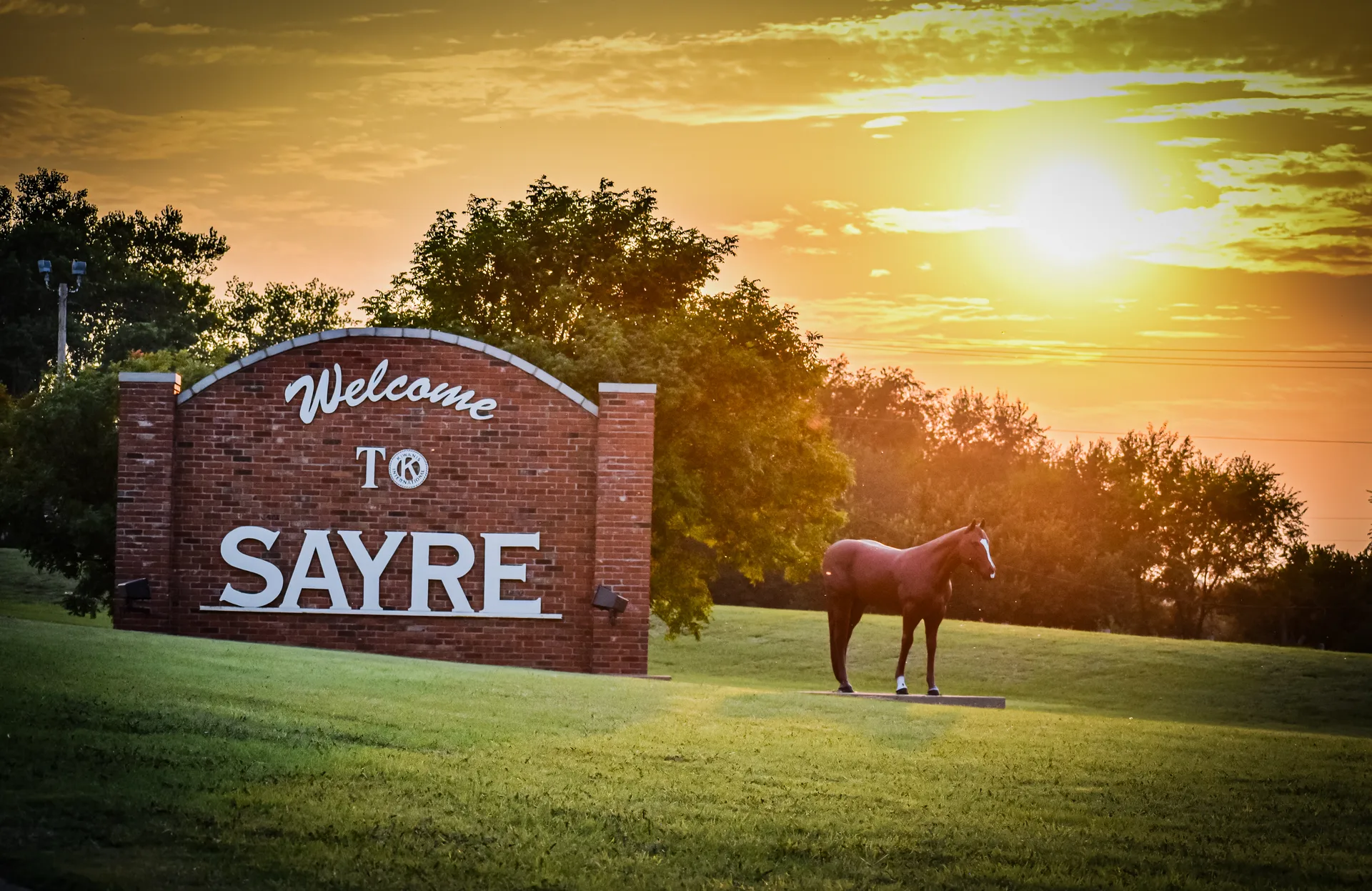 The Welcome to Sayre sign and horse sculpture at sunset.