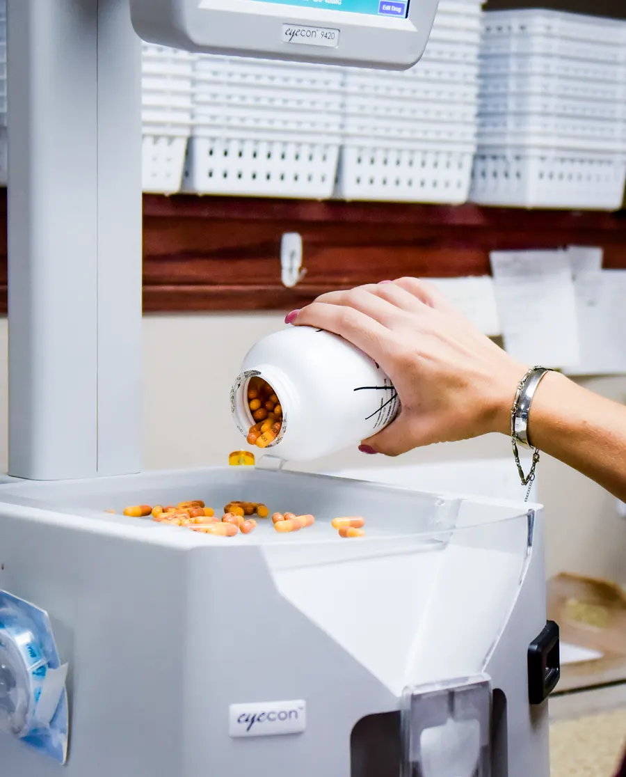 A team member pouring tablets from a medicine bottle into the pharmacy dispensing machine.