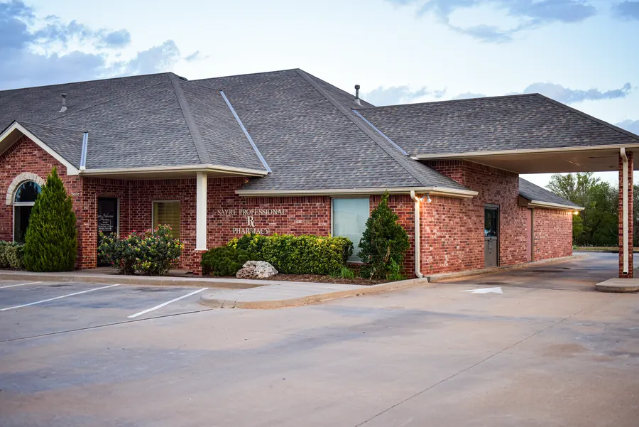 The Sayre Professional Pharmacy building and covered drive-through beside the parking area.