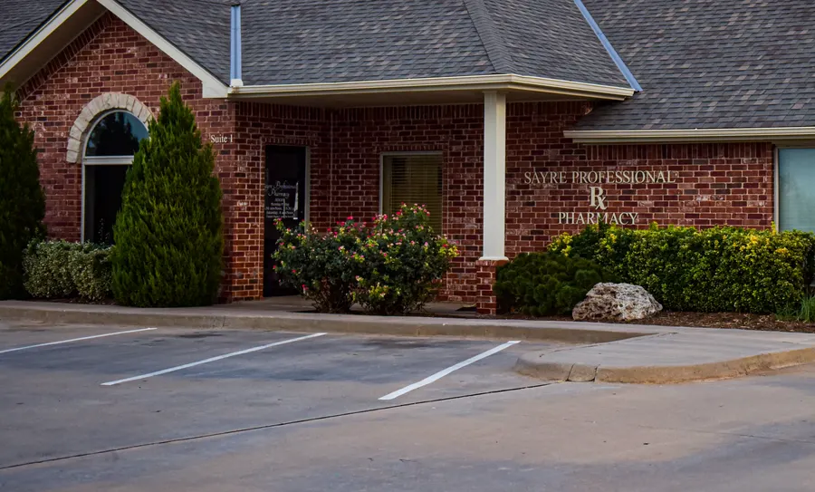 The brick entrance of Sayre Professional Pharmacy with its name above the flower beds.