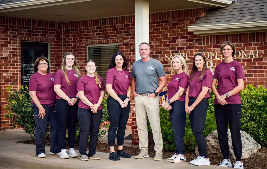 The Sayre Professional Pharmacy team standing together outside the brick pharmacy building.